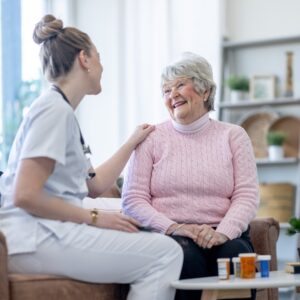 Female nurse holding the shoulder of an elderly lady. Both of them smiling at each other.